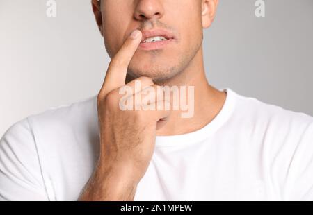 Mann mit Herpes, der Lippen vor hellgrauem Hintergrund berührt, Nahaufnahme Stockfoto