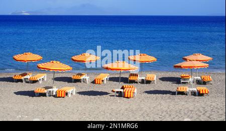 Griechenland. Die Insel Kos. Kefalos Strand. Orangefarbene Stühle und Sonnenschirme am Strand Stockfoto