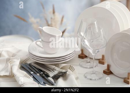 Set aus sauberem Geschirr, Besteck und Weingläsern auf weißem Holztisch Stockfoto