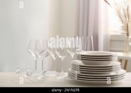 Set aus sauberem Geschirr und Weingläsern auf weißem Tisch im Innenbereich Stockfoto