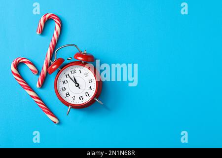 Wecker und Zuckerstangen auf hellblauem Hintergrund, flach liegend mit Platz für Text. Der Countdown für das neue Jahr Stockfoto