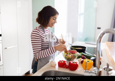 Lächelnde junge arabische Hausfrau, die zu Hause das Abendessen zubereitet Stockfoto