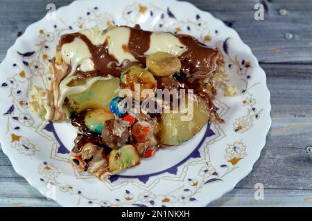 Schokoladenmischung mit Keksen und verschiedenen Arten von Schokoladenstücken und Sahne mit frischen Ananas- und Bananenstücken auf einem Teiggebäck Stockfoto