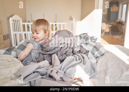 Hausreinigung. Ein glückliches kleines Mädchen, die Helferin hat Spaß und lächelt, während sie in einer hellen Wohnung ist. Hilft Eltern, die Bettwäsche zu wechseln Stockfoto