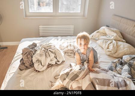 Hausreinigung. Ein glückliches kleines Mädchen, die Helferin hat Spaß und lächelt, während sie in einer hellen Wohnung ist. Hilft Eltern, die Bettwäsche zu wechseln Stockfoto