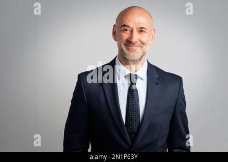 Porträt eines weißen Geschäftsmannes, der in die Kamera schaut und lächelt. Ein reifer, männlicher Profi ist in Ordnung. Er ist vor grauem Hintergrund. Stockfoto