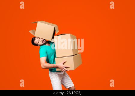 Es ist Umzugstag der vielbeschäftigte komische Typ in lässiger Kleidung trägt große Kisten in den Händen und versucht, einen mit seinem Kopf zu halten, isoliert auf gelb Stockfoto