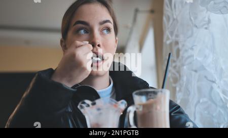 Ein Mädchen isst Eis vor einem Cappuccino in einem Café. Stockfoto