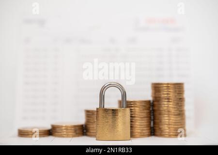 Geld- und Sicherheitskonzept. Goldenes Hauptschlüsselschloss mit einem Münzstapel auf dem Bankpassbuch. Stockfoto