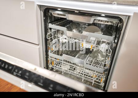 Viele schmutzige Teller in der Spülmaschine. Eingebauter Geschirrspüler mit geöffneter Tür. Haushaltsgerät Geschirrspülmaschine in moderner Küche. Weißton und Stockfoto