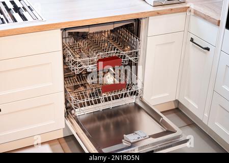 Leere eingebaute Geschirrspüler mit geöffneter Tür. Haushaltsgerät Geschirrspülmaschine in moderner Küche. Weiße Farbtöne und saubere Küche. Stockfoto