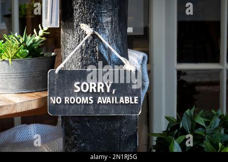 Ein Schild mit der Aufschrift „Sorry, No Vacancy“ hängt vor einem Gelände in einem britischen Strandresort. Das Schild steht draußen, um anzuzeigen, dass keine Zimmer verfügbar sind Stockfoto