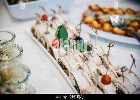 Eine Nahaufnahme des gewickelten Canapés in weißem Servierteller auf dem Tisch mit unscharfem Hintergrund Stockfoto