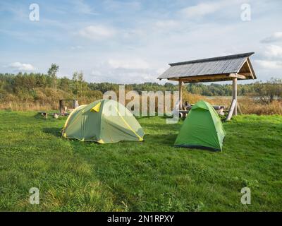 Zwei grüne Touristikzelte stehen im Camp. Holztisch, Bänke und Feuerstelle zum Campen. Wandern in Russland. Stockfoto