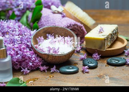Spa-Ambiente mit natürlicher Seife, fliederfarbenem ätherischen reinen Öl, Meersalz und Massagesteinen mit weichen Baumwollhandtüchern zum Verwöhnen Stockfoto
