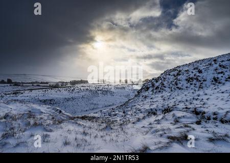 Die schneebedeckte Südseite von Peel Crag mit Blick auf die B6318, Northumberland National Park, England Stockfoto