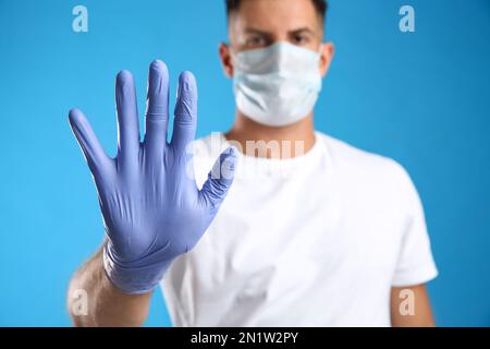Mann in Schutzmaske und medizinische Handschuhe zeigen Stop-Geste vor blauem Hintergrund, Fokus auf Hand Stockfoto