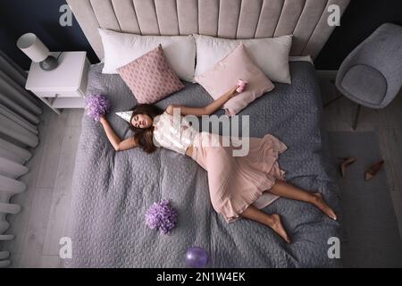 Erschöpfte Frau in festlichem Outfit, die zu Hause nach der Party im Bett schläft, über der Aussicht Stockfoto