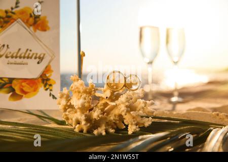 Korallen mit Goldringen und Hochzeitseinladungen am Sandstrand Stockfoto