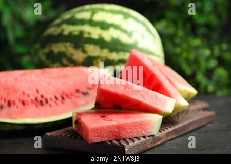 Ganze und geschnittene reife Wassermelonen auf schwarzem Tisch Stockfoto