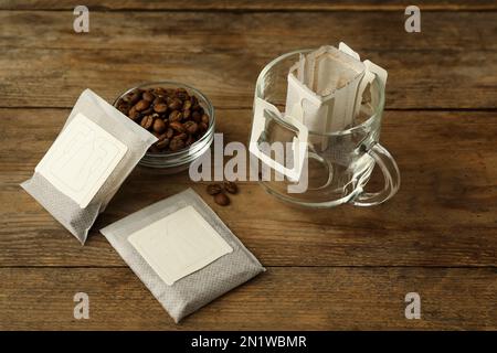 Tropfen Sie Kaffeebeutel, Bohnen und Glasbecher auf einen Holztisch Stockfoto