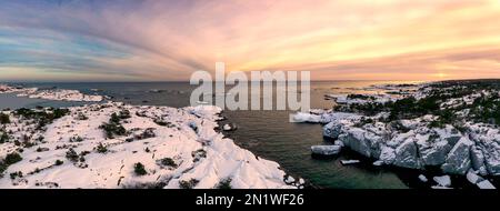 Luftaufnahme der verschneiten Küste am Meer, farbenfroher Himmel bei Sonnenuntergang in Norwegen. Wintersonnenlandschaft mit frostigem Meer, Fjord und Horizont. Draufsicht. Stockfoto