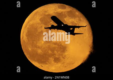 London, Großbritannien. 6. Februar 2023 Das Flugzeug fliegt durch den Mond. Ein Passagierjet, der vom Flughafen London City abhebt, durchquert einen 99,1% Vollmond, der über der Stadt aufsteigt. Kredit: Guy Corbishley/Alamy Live News Stockfoto