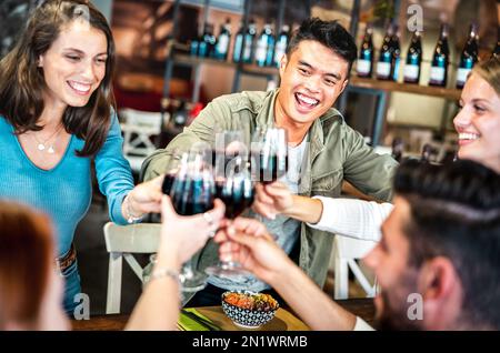 Trendige multikulturelle Freunde, die Rotwein im Sushi Poke Bowl Restaurant anstoßen - Lifestyle-Konzept für Speisen und Getränke mit fröhlichen Menschen, die Spaß haben Stockfoto