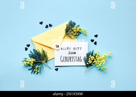 Text Alles Gute zum Geburtstag bedeutet Happy Birthday in deutscher Sprache. Text Special Moments auf Papierkarte mit Mimosablüten in gelbem Umschlag auf m Stockfoto