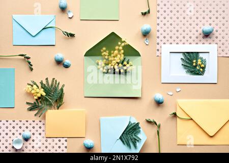 Osterhintergrund mit Wachteleiern. Mimosa- und Freesia-Blumen, mintgrüne Umschläge und farbiges Papier auf gelbem Hintergrund. Flach liegend, über Kopf, knurrt Stockfoto