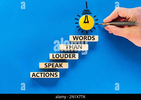 Das Symbol „Aktionen sprechen lautere Wörter“. Begriffe Taten sprechen lauter als Worte auf Holzblöcken. Wunderschöner blauer Hintergrund. Geschäftsmannshand. Busine Stockfoto