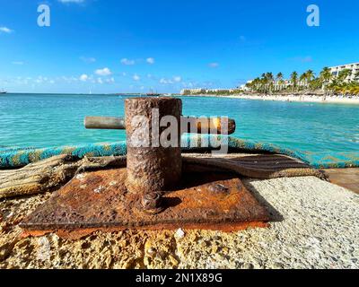 Nahaufnahme eines alten, verrosteten Pollens auf einem Pier in Aruba. Das karibische Meer und Palm Beach im Hintergrund. Stockfoto