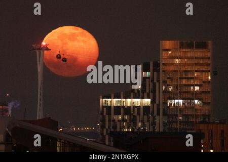 London, Großbritannien. 6. Februar 2023 UK Weather: 99,1 % Vollmondaufgang erzeugt Silhouetten von vorbeifahrenden Seilbahnen, auch als IFS Cloud Cable Car im Osten Londons bekannt. Kredit: Guy Corbishley/Alamy Live News Stockfoto