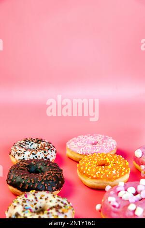 Doughnuts mit mehrfarbiger Glasur in zwei Reihen auf trendigen pinkfarbenen Hintergrund. Donuts sind traditionelle süße Gebäckstücke. Platz für Text kopieren. Stockfoto