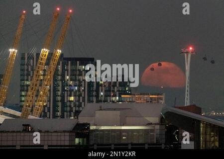 London, Großbritannien. 6. Februar 2023 UK Weather: 99,1 % Vollmondaufgang erzeugt Silhouetten von vorbeifahrenden Seilbahnen, auch als IFS Cloud Cable Car im Osten Londons bekannt. Kredit: Guy Corbishley/Alamy Live News Stockfoto