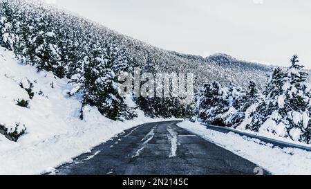 Schneebedeckte Bergstraße, umgeben von Schnee. Winterlandschaft mit schneebedeckten Bäumen und schneebedeckten Wäldern. Immergrüner Fichtenwald. Alpenlandschaft. Urlaub, Stockfoto