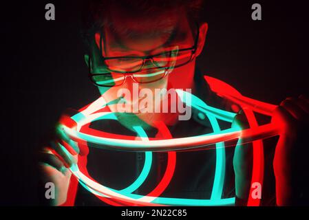 Glitch Double Exposure futuristisches Porträt in attraktivem jungen Hipstermann mit trendigen Brillen, eingewickelt mit Neon-Leuchtband in Neonlicht Stockfoto