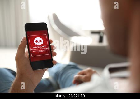 Mann mit Smartphone mit Warnung vor Virenangriff zu Hause, Nahaufnahme Stockfoto