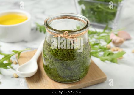 Ein Glas mit leckerem Rucola-Pesto und Zutaten auf dem weißen Tisch Stockfoto