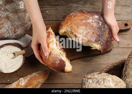 Eine Frau bricht frisch gebackenes Brot am Holztisch, Nahaufnahme Stockfoto