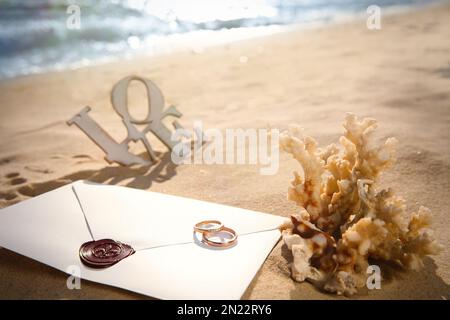 Umschlag, goldene Eheringe und Korallen am Sandstrand Stockfoto