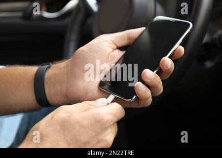 Mann, der im Auto das Ladekabel mit dem Smartphone verbindet, Nahaufnahme Stockfoto