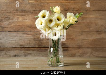 Wunderschöne weiße Eustoma-Blumen in Vase auf dem Tisch vor Holzhintergrund Stockfoto