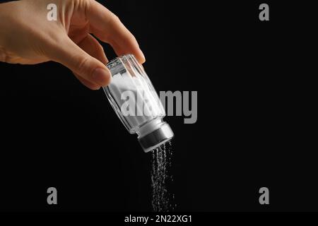 Eine Frau, die Salz aus dem Shaker schüttelt, auf schwarzem Hintergrund, Nahaufnahme Stockfoto