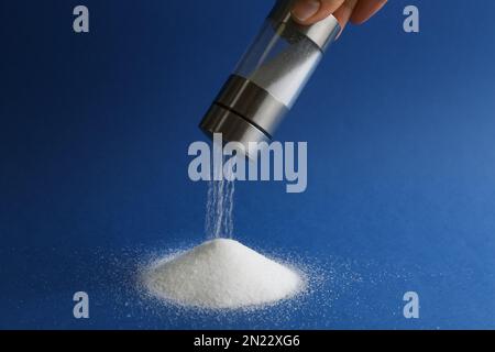 Eine Frau, die Salz aus dem Shaker schüttelt, auf blauem Hintergrund, Nahaufnahme Stockfoto