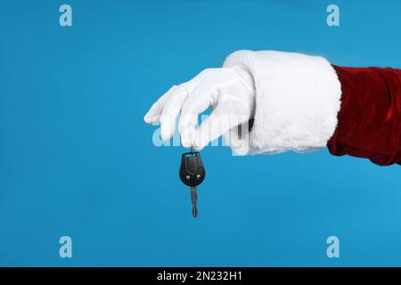 Der Weihnachtsmann hält den Autoschlüssel auf blauem Hintergrund, Nahaufnahme der Hand Stockfoto