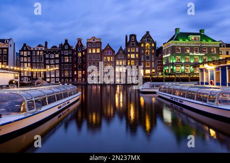 AMSTERDAM, NIEDERLANDE - 18. JANUAR 2023: Stadtbild traditioneller holländischer Häuser bei Sonnenuntergang am Damrak-Kanal in Amsterdam Stockfoto
