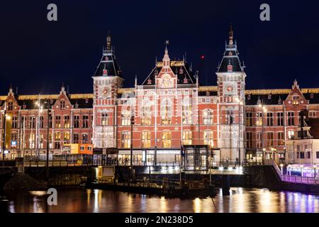 AMSTERDAM, NIEDERLANDE - 18. JANUAR 2023: Skyline von Amsterdam bei Nacht am Hauptbahnhof und Anlegestelle für Touristenboote. Stockfoto