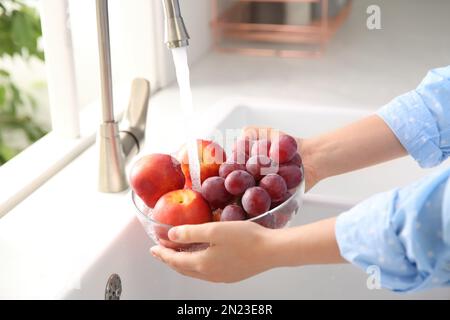 Eine Frau wäscht frische Trauben und Nektarinen in der Küchenspüle Stockfoto