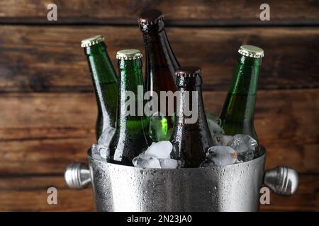 Metalleimer mit Flaschen Bier und Eiswürfeln auf Holzhintergrund, Nahaufnahme Stockfoto